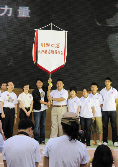 黎明及香港志願者協會副主席林亨利先生從亞組委志願者部宣傳策劃辦公室副主任呂娜(右七)手中接過廣州亞運會志願者旗幟後，高高舉起。右八為廣播處長黃華麒先生。